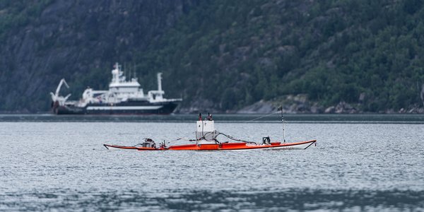 

En kajakkdrone på fjorden med et forskningsfartøy i bakgrunnen