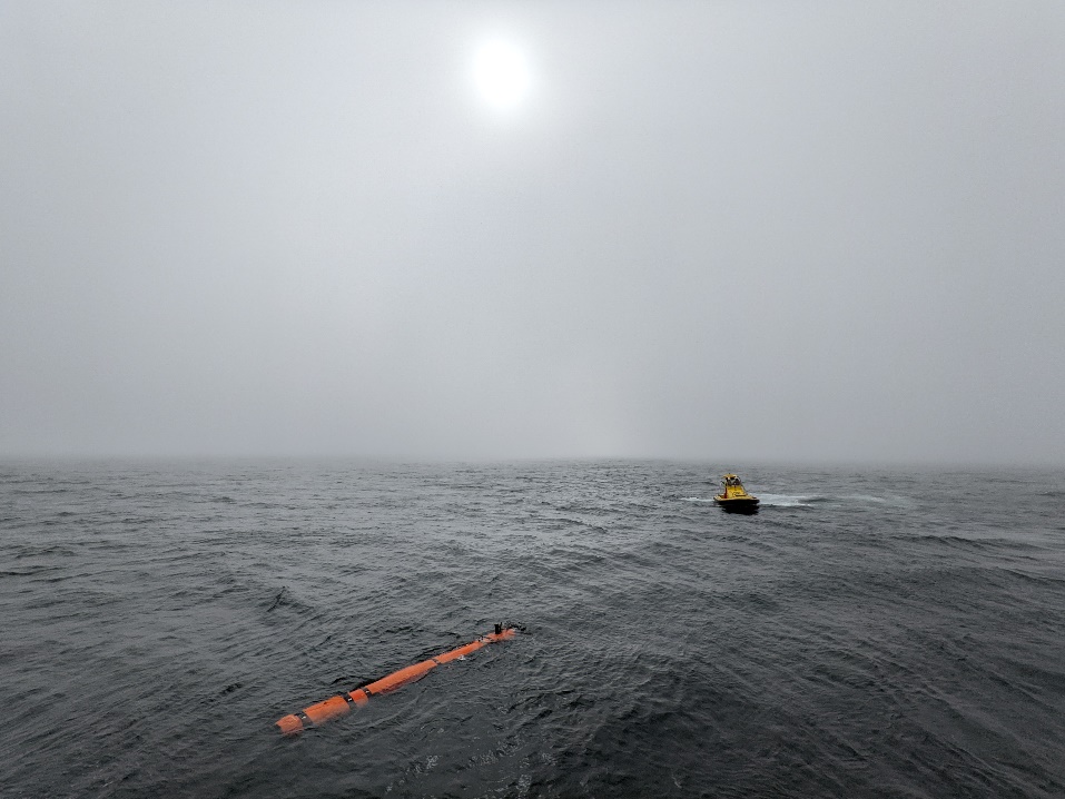 Photo of the AUV and MOB boat on calm water with fog obscuring the circle of the sun