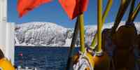 

Bilde tatt fra dekk på en båt. I sjøen flyter det merker fra en utsatt bøye. Snødekte fjell i bakgrunnen.